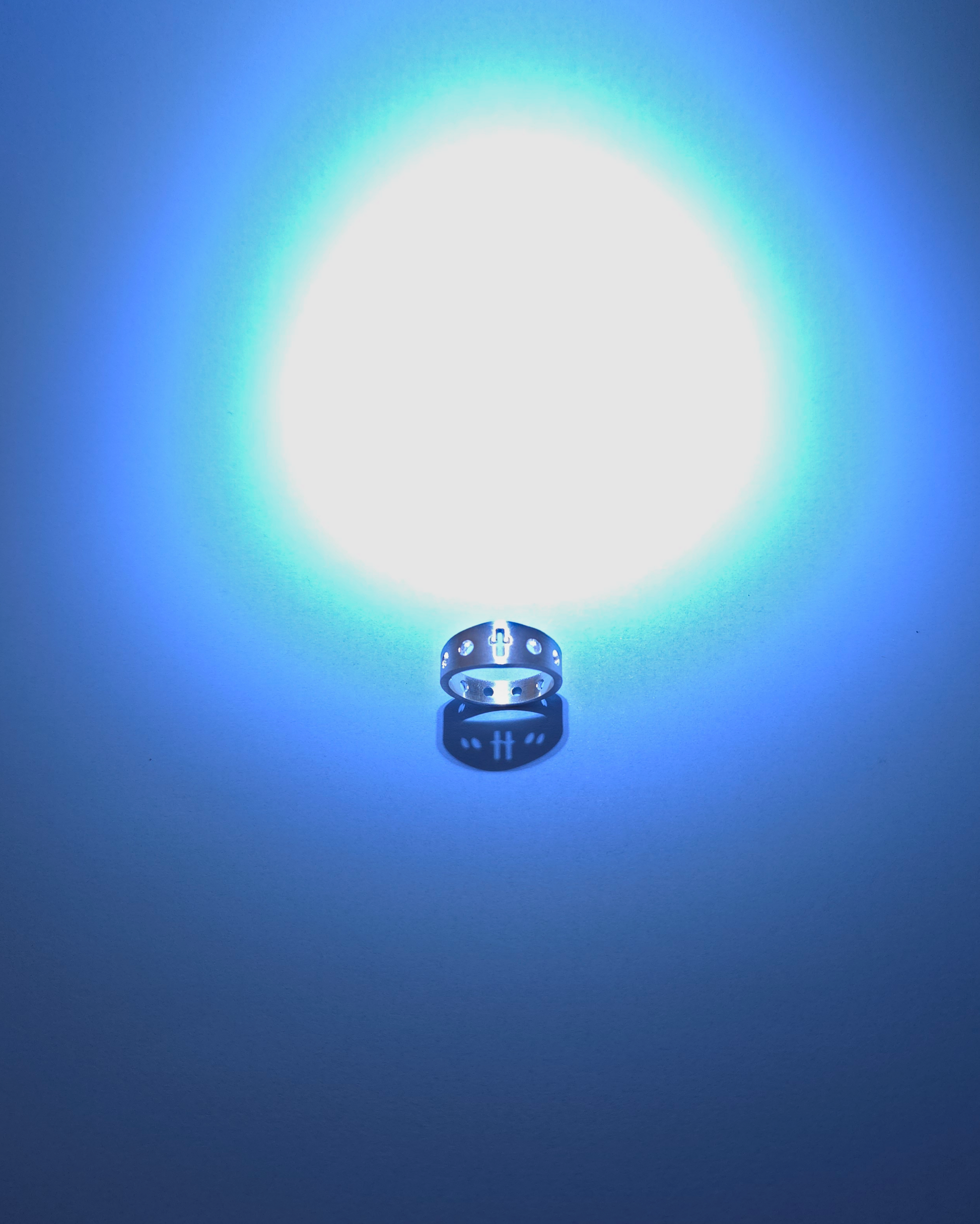 silver rosary ring with a massive ball of light above it, on a blue backdrop.